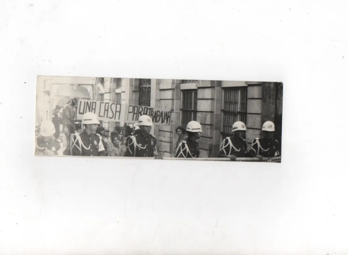 Impresa fotográfica en blanco y negro: cascos de la policía frente a la carpa de La Mama